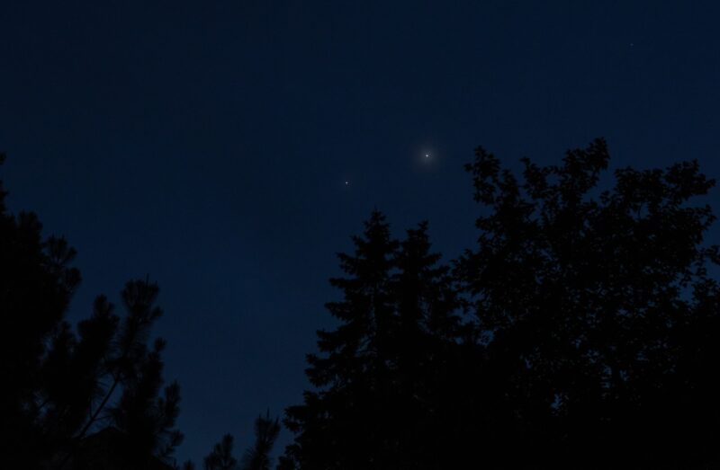 2 dim dots in an almost black sky, above tall trees.