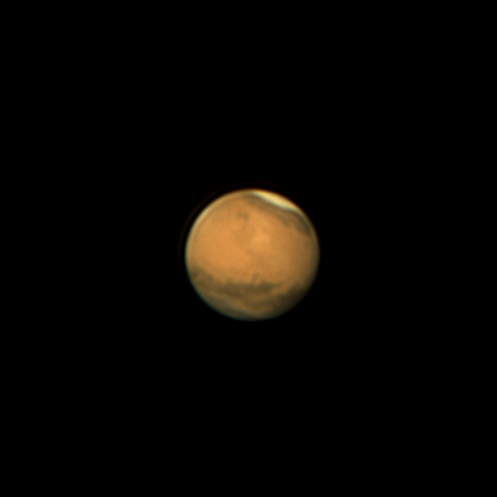 Reddish Mars showing dark spots and a lighter colored area on top.