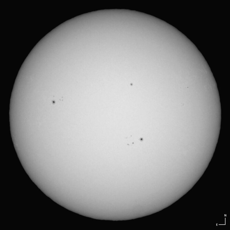 The sun, seen as a large white sphere with small dark spots.