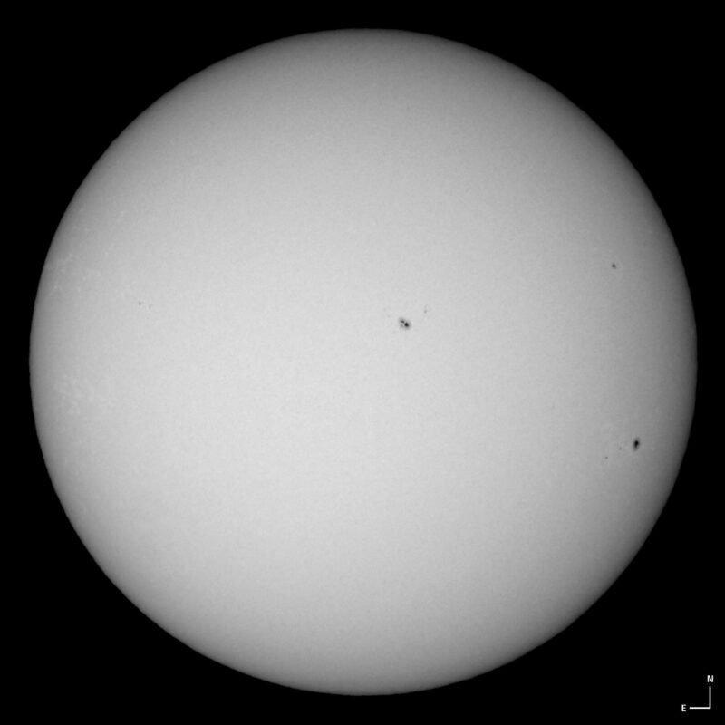 The sun, seen as a large white sphere with small dark spots.