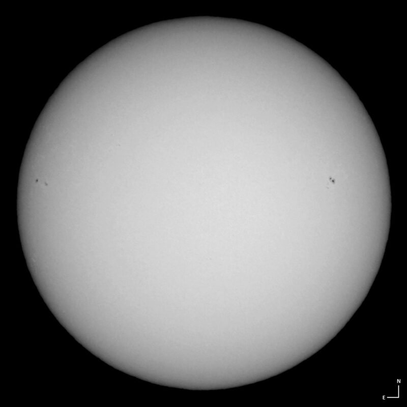 The sun, seen as a large white sphere with small dark spots.