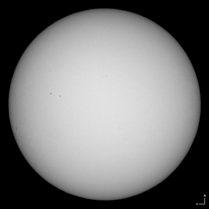The sun, seen as a large white sphere with small dark spots.