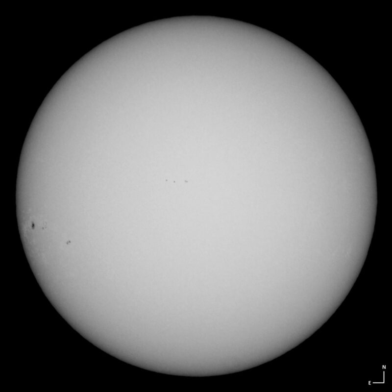 The sun, seen as a large white sphere with small dark spots.