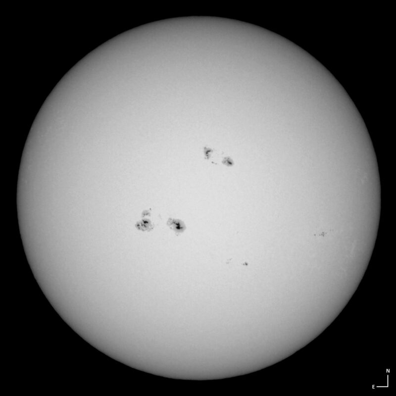 The sun, seen as a large white sphere with small dark spots.