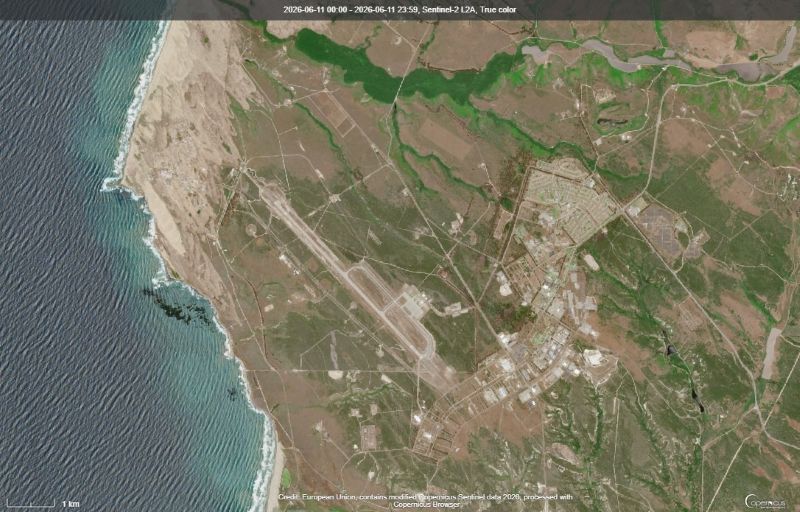 View from space at a coast on the left and an airstrip and buildings on the right.