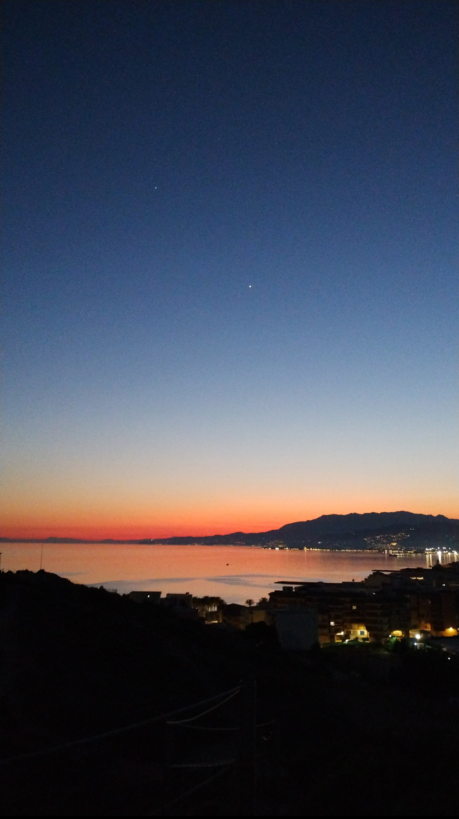 Dark blue sky and orange horizon reflecting on the coast below. Two bright dots stand out in the sky.