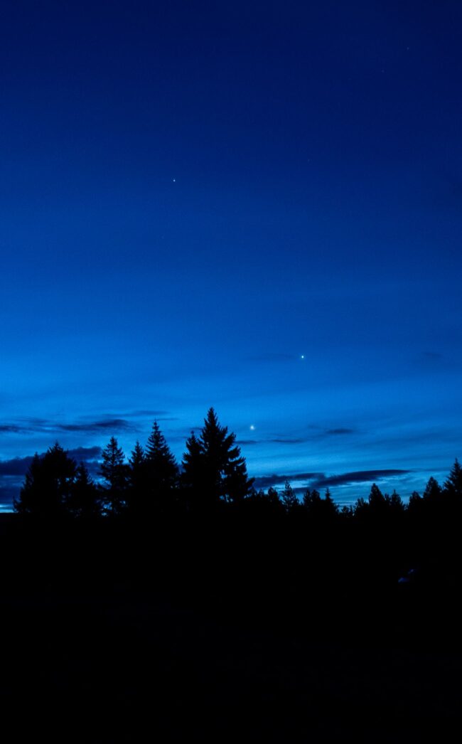 Electric blue sky with very bright dots visible. Many trees below.