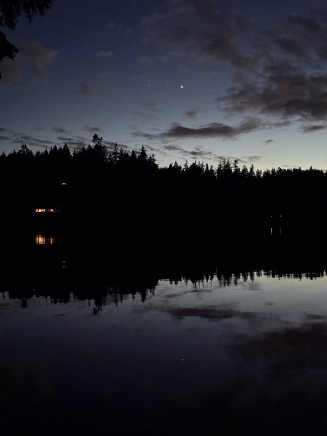 Bright dots in a slightly cloudy sky. The dots and clouds are reflected in the water below.