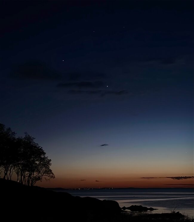 Dark sky with a orange horizon. There are 2 bright dots in the center and 2 fainter dots at top and 1 at bottom right.