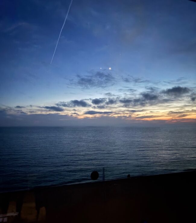 2 bright dots high in the dark blue sky. There are some clouds over the orange horizon.