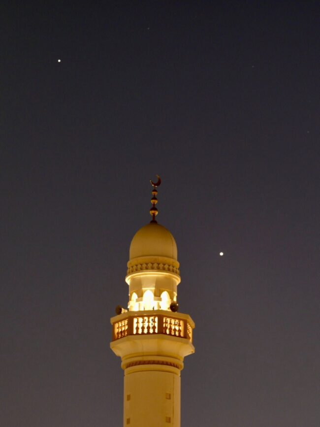Long, thin building with the shape of a waxing crescent moon at the top. It forms a line with 2 bright dots on either side.
