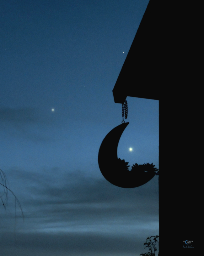 Ornament with a waning crescent shape hanging from a roof. Venus is inside the moon shape, Jupiter is to the top left.