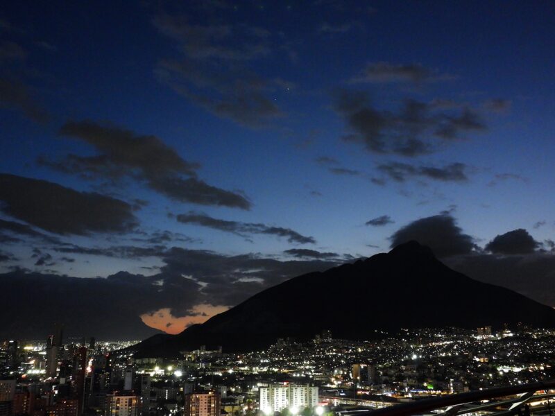 2 tiny dots of light in a vast sky. With a large city below. There is a big mountain to the right side.