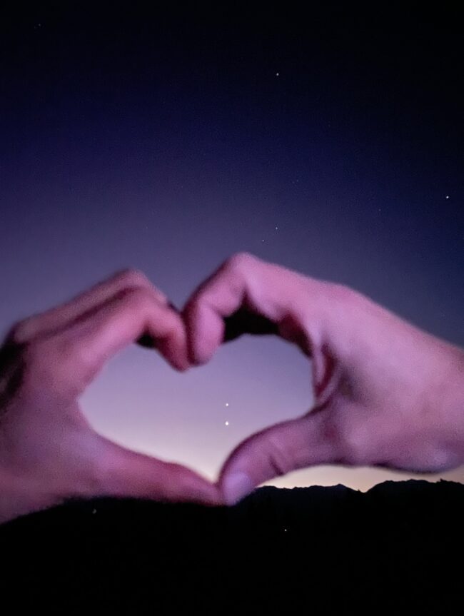 Two hands together form the shape of a heart. Two bright dots are located inside the shape.
