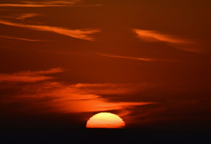Half sun in an orange sky. The sun looks orangish near the bottom and yellowish at the top.
