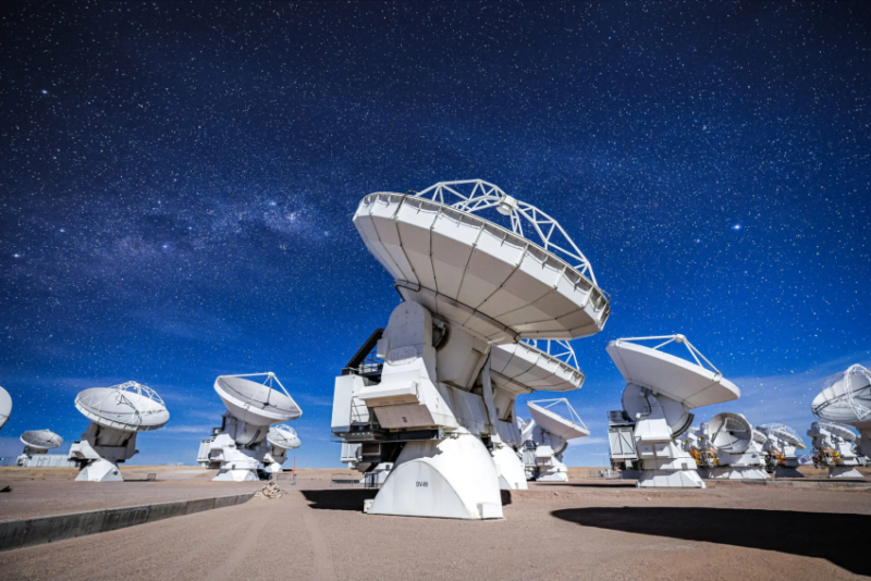 Alien intelligence search: 11 big white dish-shaped radio receivers on top of columns of machinery under a starry sky.