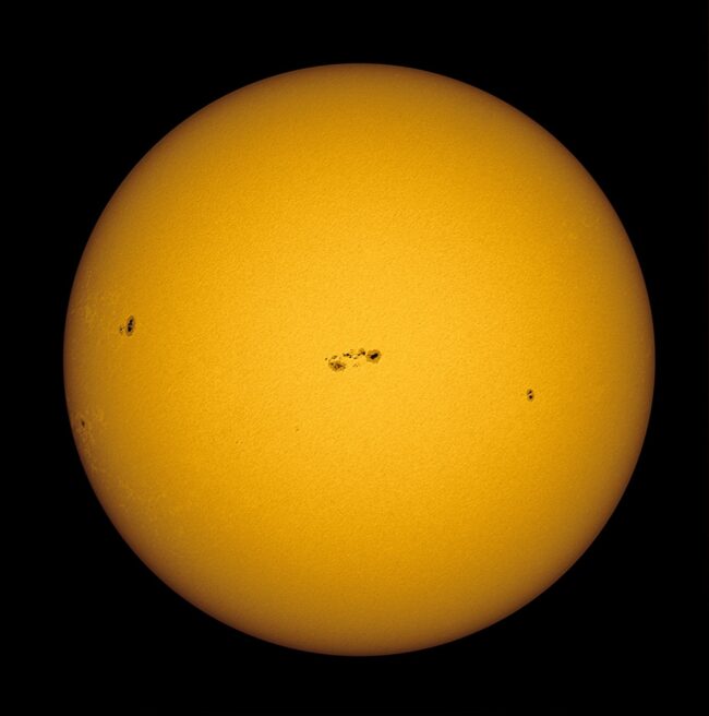 The sun, seen as a large yellow sphere with small dark spots.