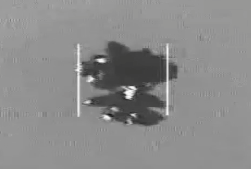 Dark object on gray background with a main body and several smaller pieces extending from the sides and bottom.