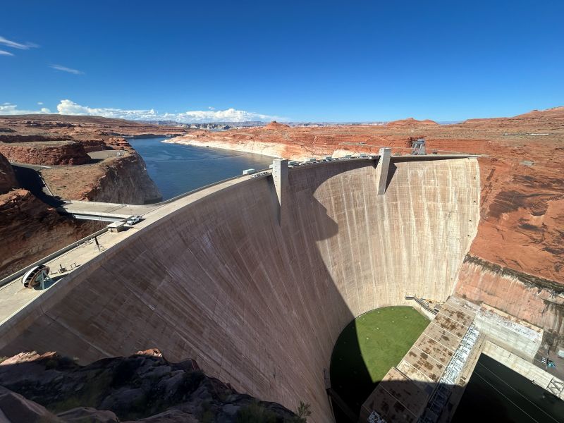 Huge arc-shaped concrete dam with water backed up behind it, in a desert.