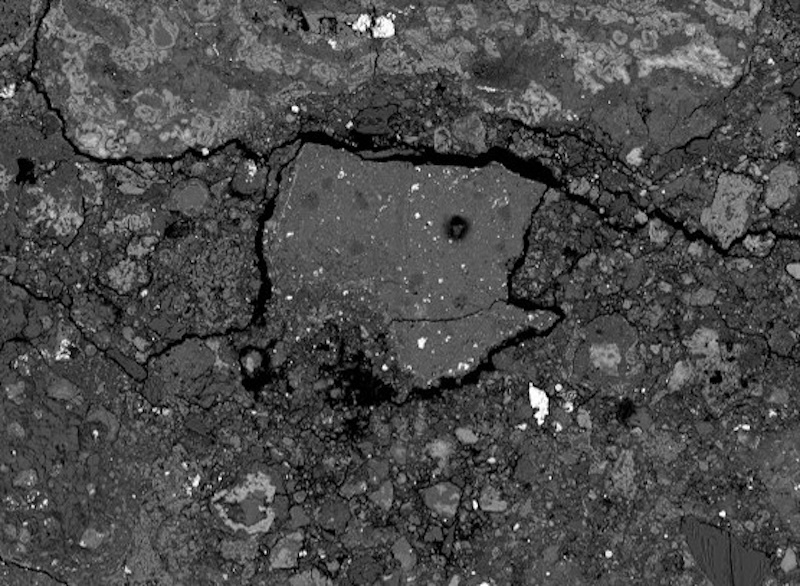 A gray rock made of small rocks stuck together, 1 bigger chunk in the middle and many white flecks.