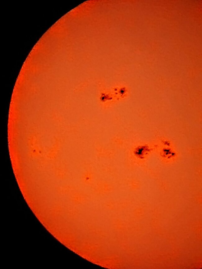 The sun, seen as an orange sectional sphere with dark spots.