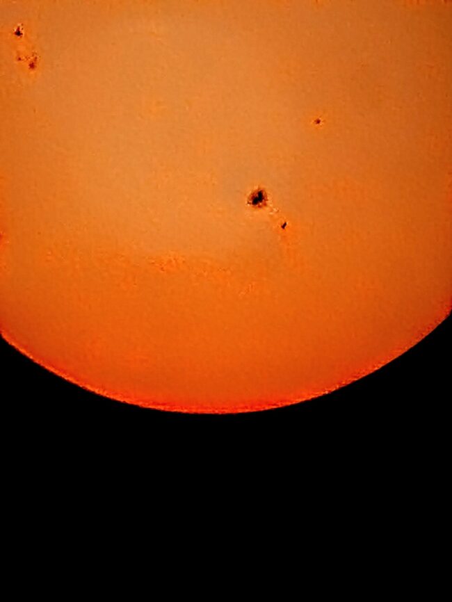 The sun, seen as an orange sectional sphere with dark spots.