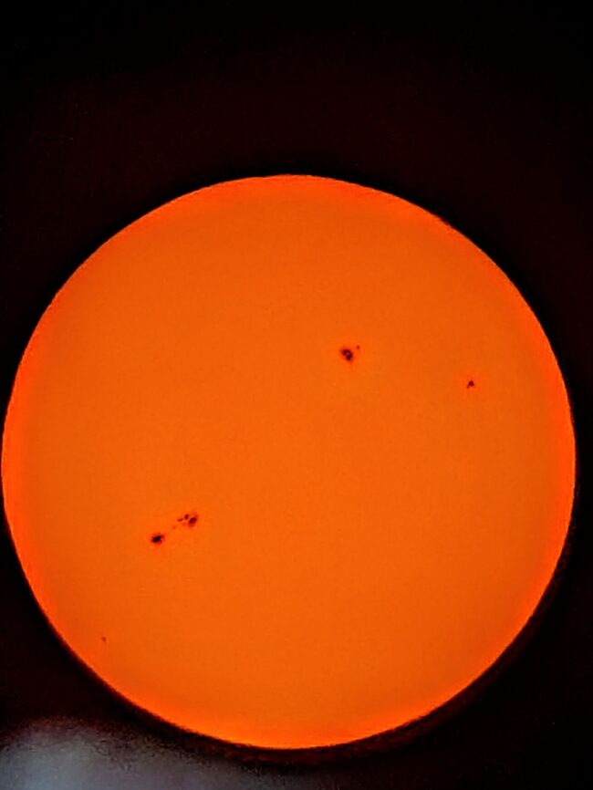 The sun, seen as an orange sectional sphere with dark spots.