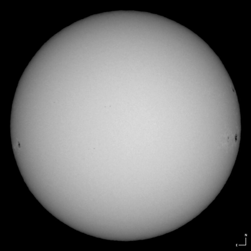 The sun, seen as a large white sphere with small dark spots.