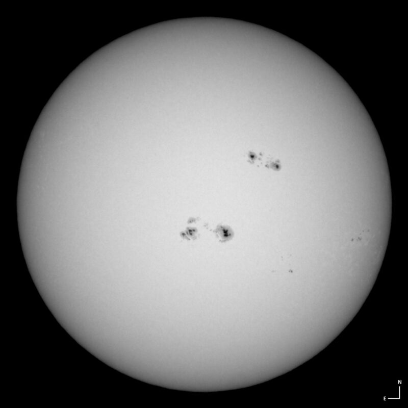 The sun, seen as a large white sphere with small dark spots.