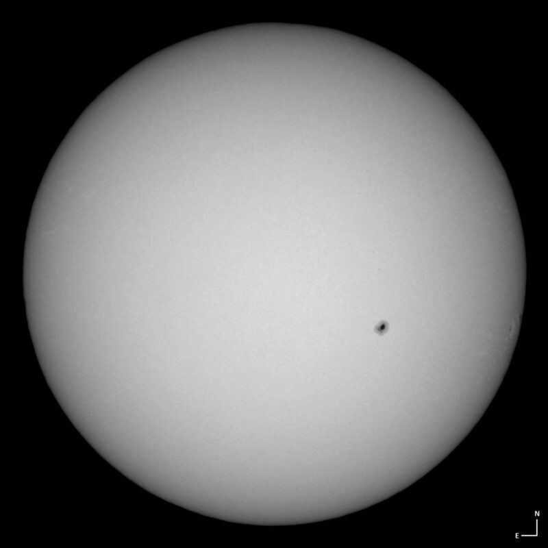The sun, seen as a large white sphere with small dark spots.