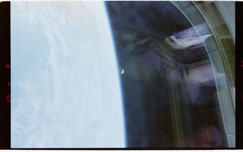 View of Earth through window on spacecraft. A small triangular object is in the distance.