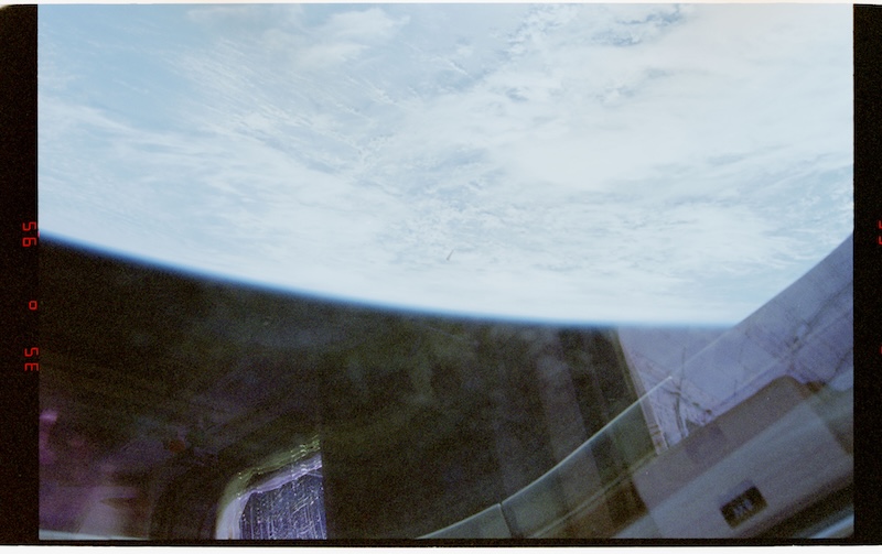 View of Earth through window on spacecraft. A small triangular object is in the distance.