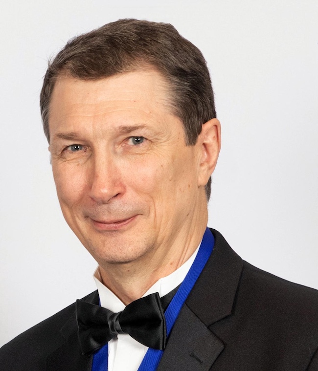 Smiling man wearing a black suit jacket, white shirt and black bow tie.