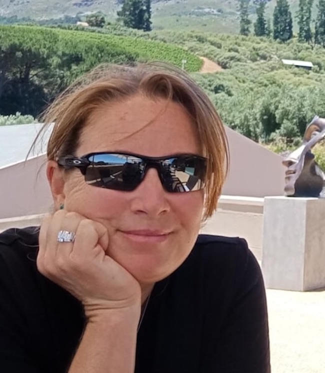 Smiling woman wearing sunglasses, with her chin resting in her hand.