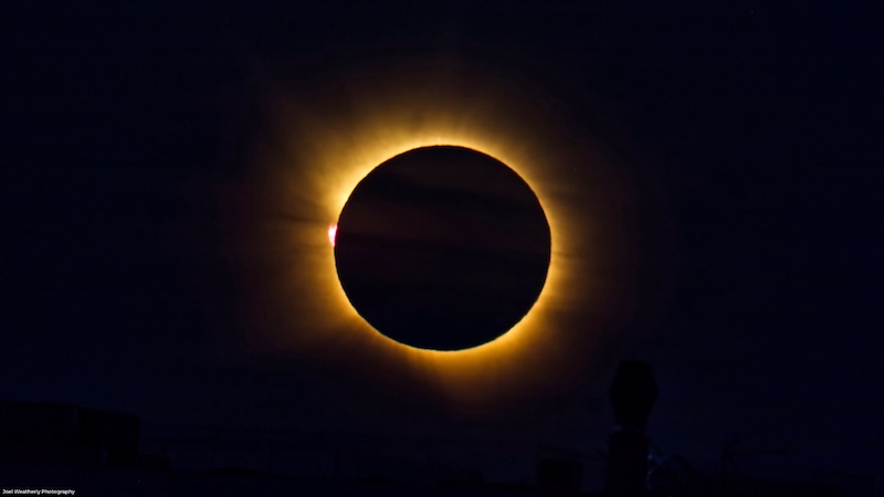 A large solid black disk surrounded by a luminous aura of golden light.