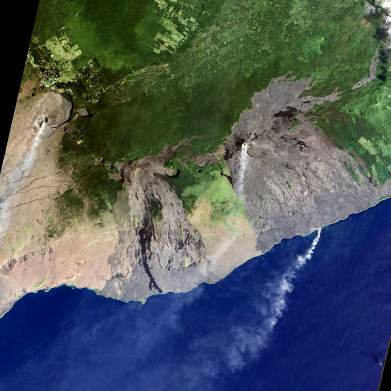 Brown and green land with 3 plumes of smoke and a deep blue ocean at the bottom.
