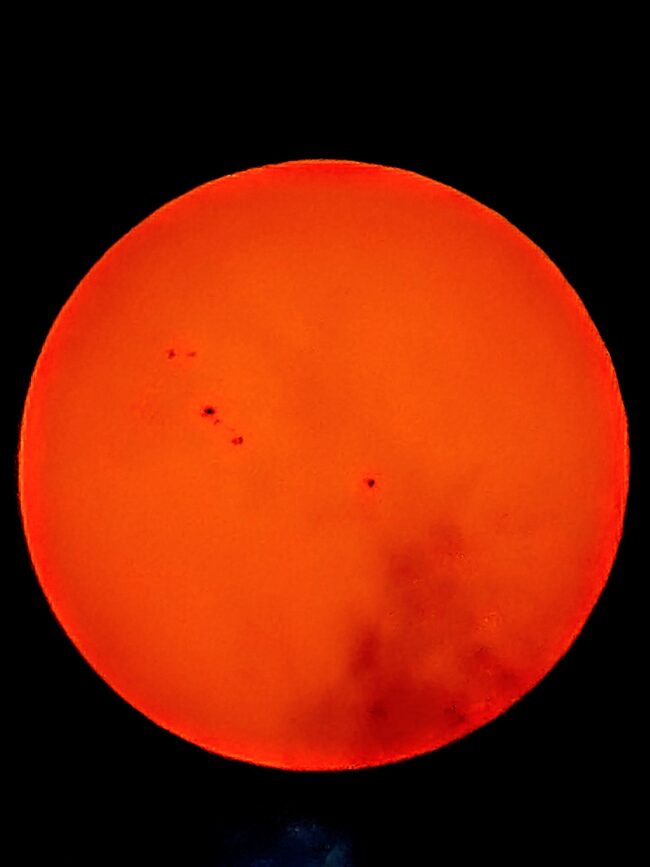 The sun, seen as a large orange sphere with dark spots.