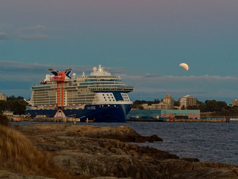 Partial lunar eclipse seen over a harbor, with a large boat in the foreground.