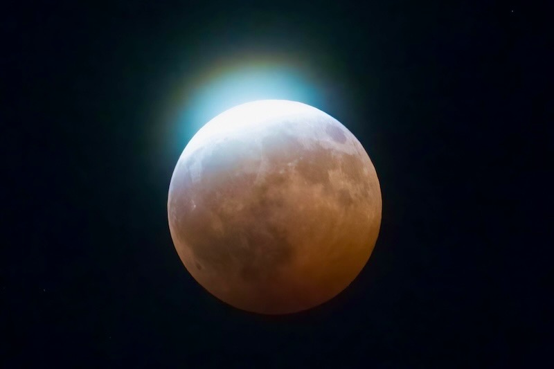 Almost totally eclipsed moon, with a slim portion of daylight showing at the top.