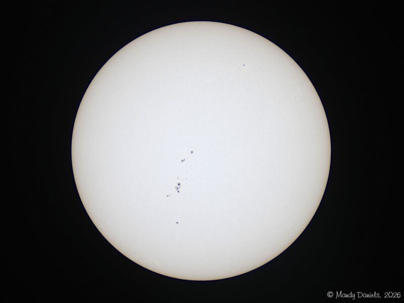 The sun, seen as a large white sphere with small dark spots.