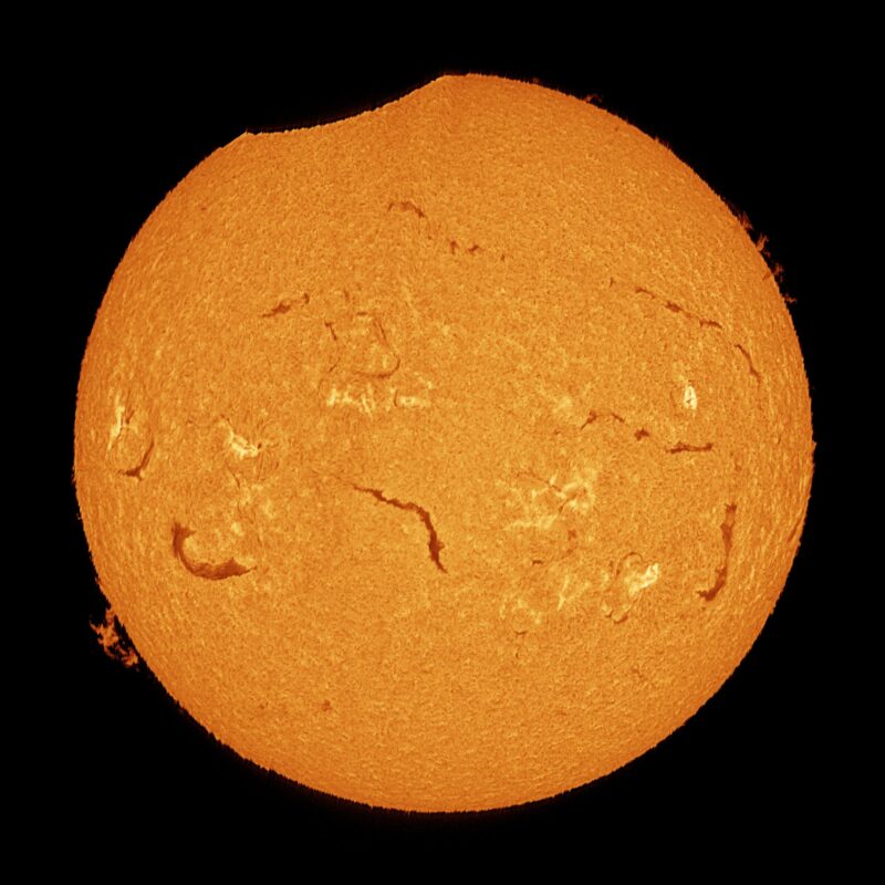 The sun, seen as a large yellow sphere with a mottled surface and a dent at the top edge.