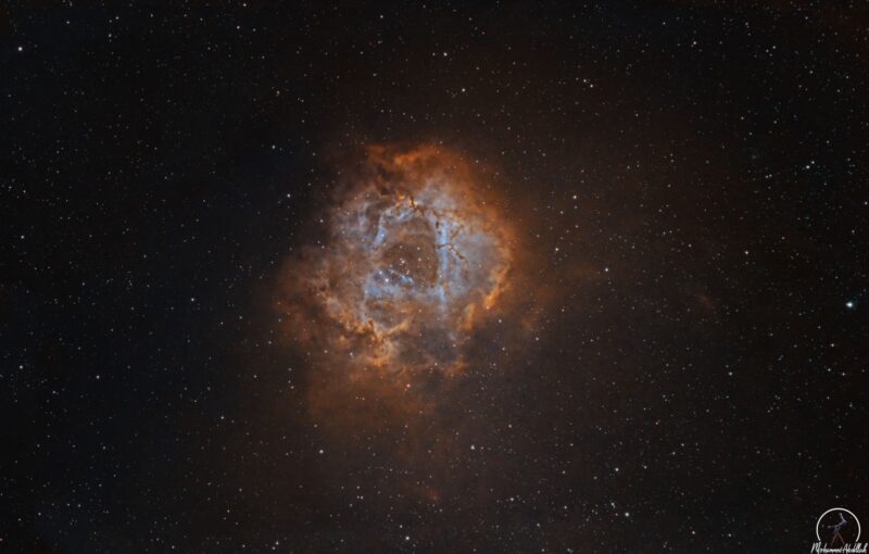 A large, spherical and hollowed-out cloud of orange and light blue, with numerous surrounding stars.