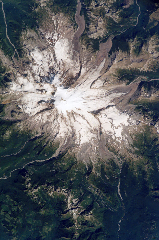 A mountain peak covered in snow with many streams coming down the flanks.