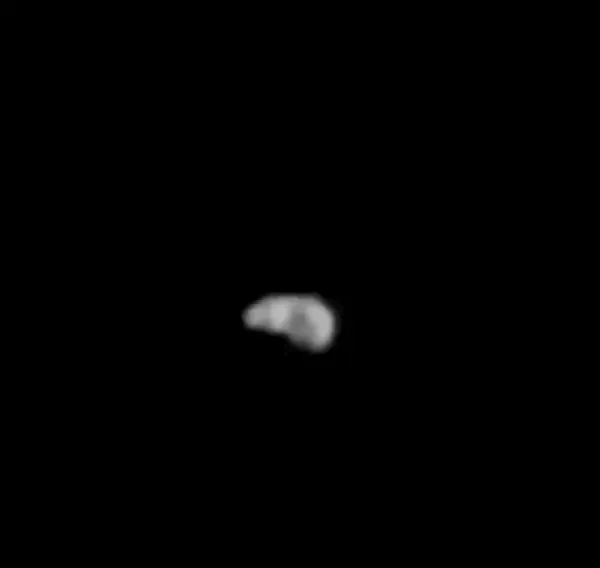 A small, white, lumpy space rock spinning in black space.