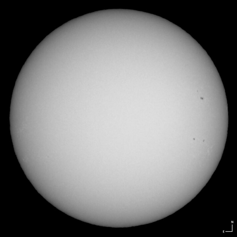 The sun, seen as a large white sphere with small dark spots.