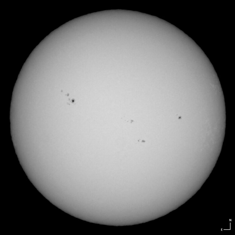 The sun, seen as a large white sphere with small dark spots.