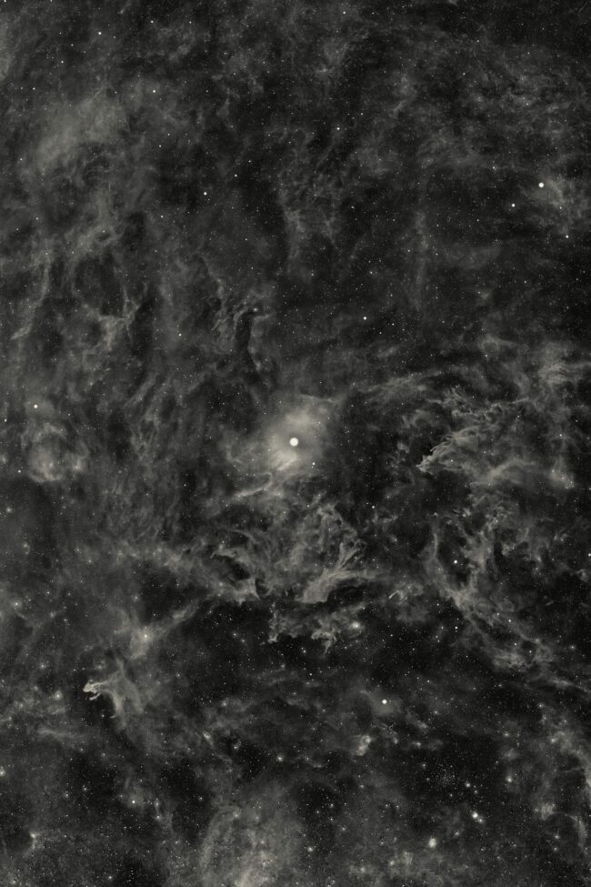 Extensive swirls of nebulosity, rendered in monochrome, with a bright central star and numerous faint stars.