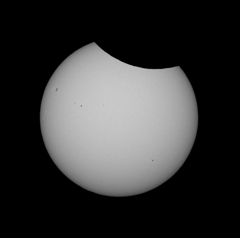 The sun, seen as a large white sphere with small dark spots.