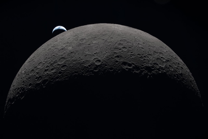 Dark gray moon partly in shadow in foreground, with distant crescent Earth beyond it.