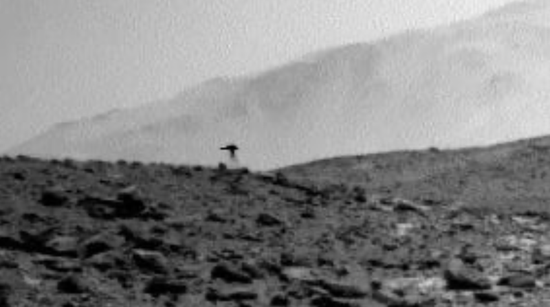 Fuzzy black and white view of a rocky hill, with a dark jellyfish-like shape on top of it.